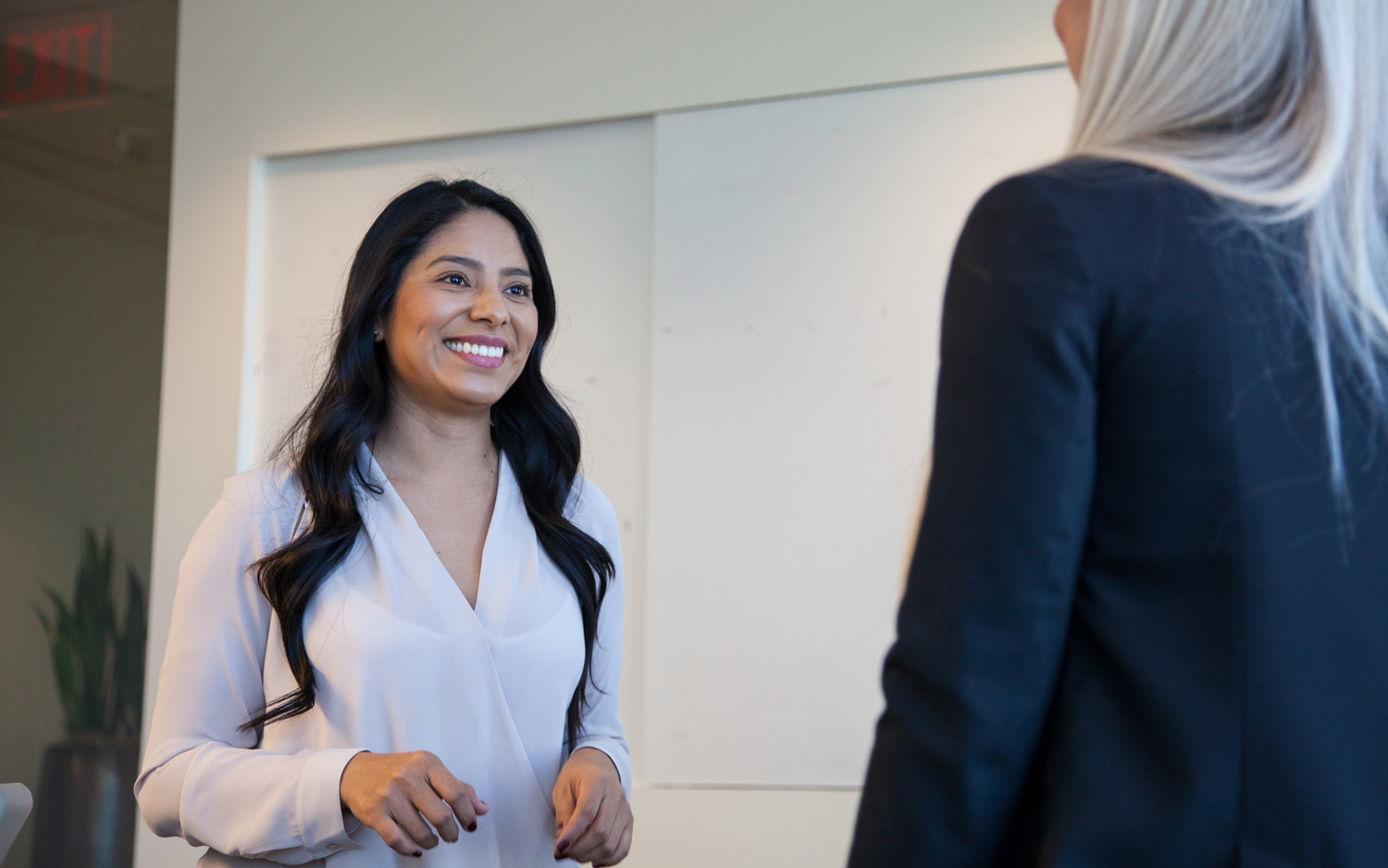 A subject in a white blouse smiles at another subject.