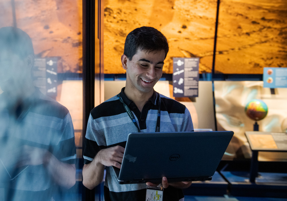 An IT student smiles as he looks at his laptop.