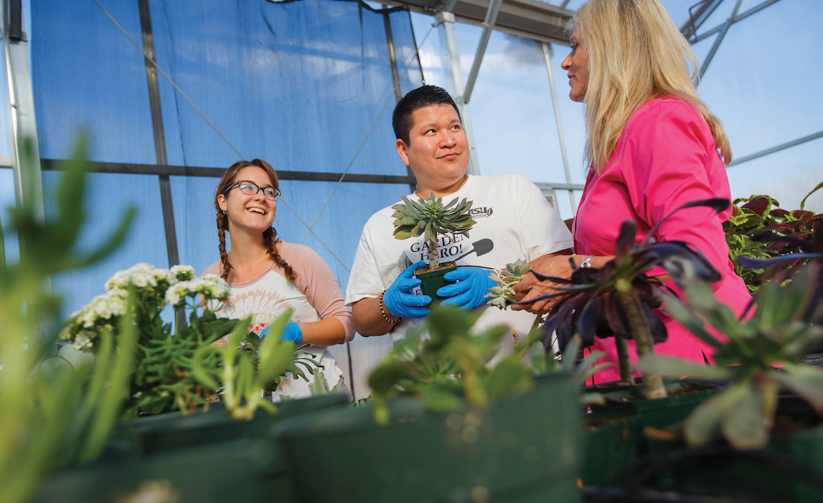 Two sustainability students smile at their professor as they work together in a garden.