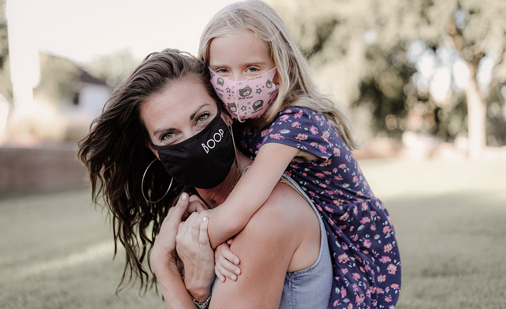 A woman and a child pose for a picture while wearing masks. 