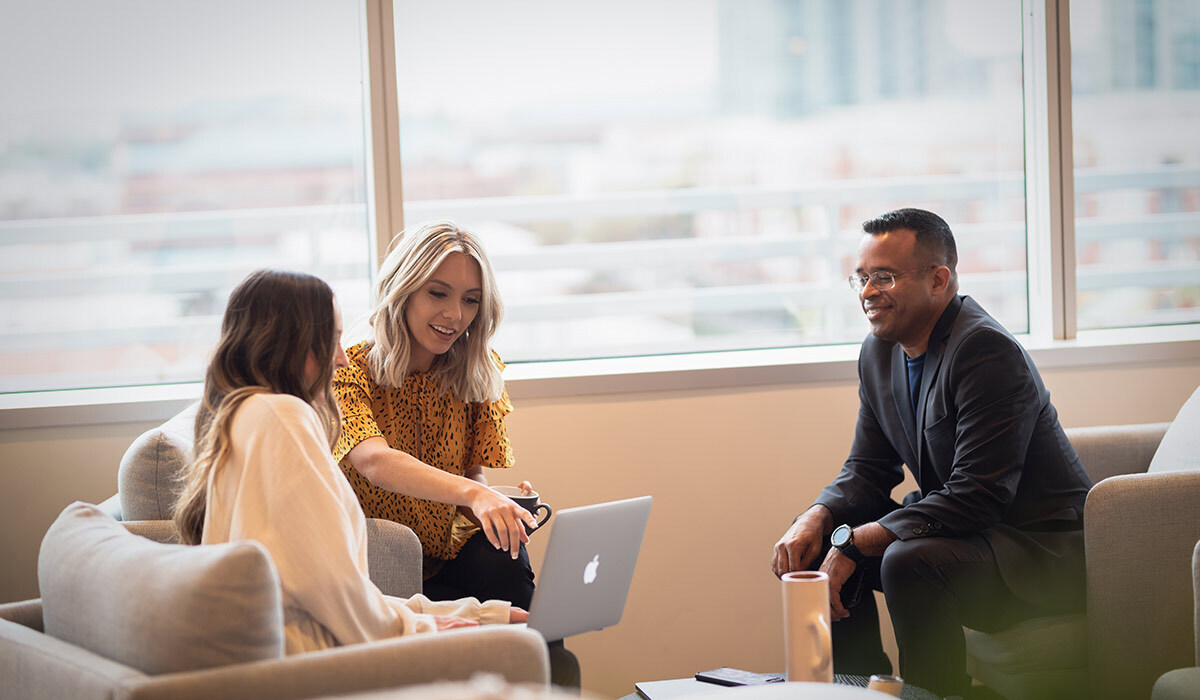 Three corrections management professionals collaborate and work on a laptop.