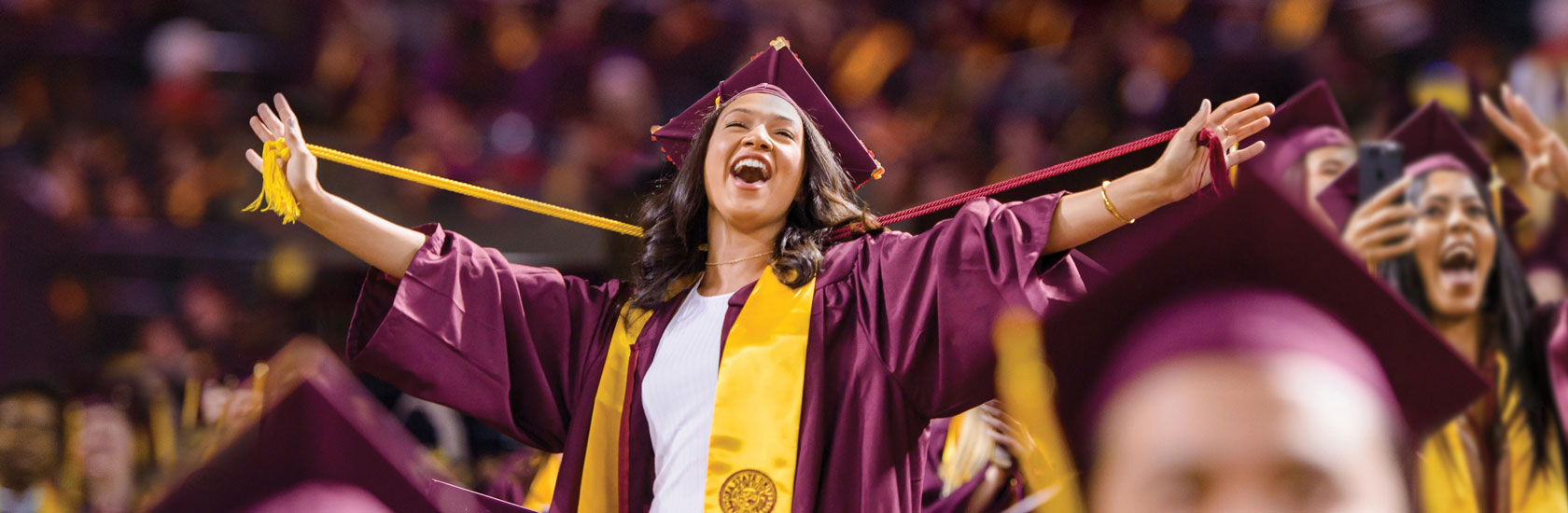 An ASU graduate cheers and holds onto her honor cords at a graduation ceremony.