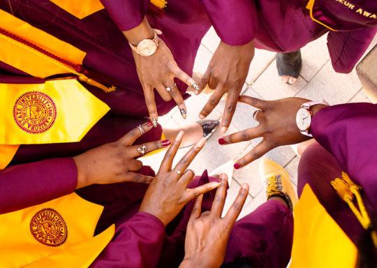 A group of ASU graduates stand in a circle showing the pitchfork hand sign.