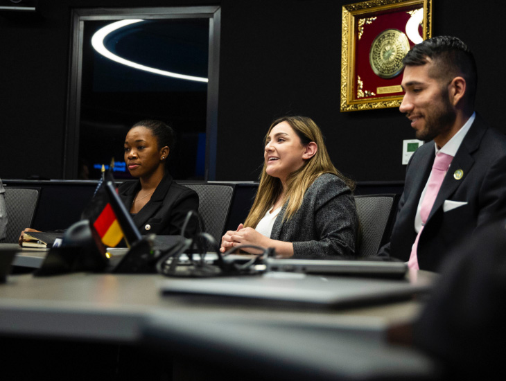 Three ASU public service students in suits smile while sitting down at a panel desk.