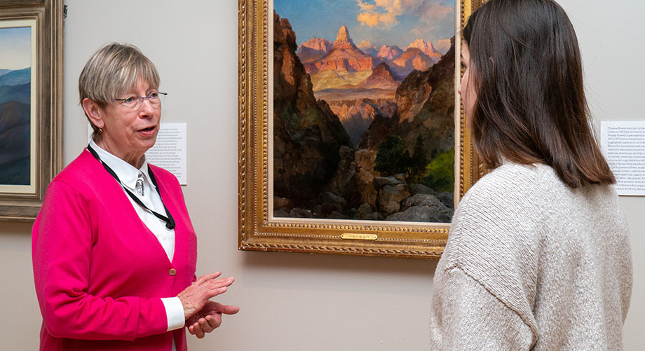 ASU professor Betsy Fahlman speaks to a student while standing next to a painting.