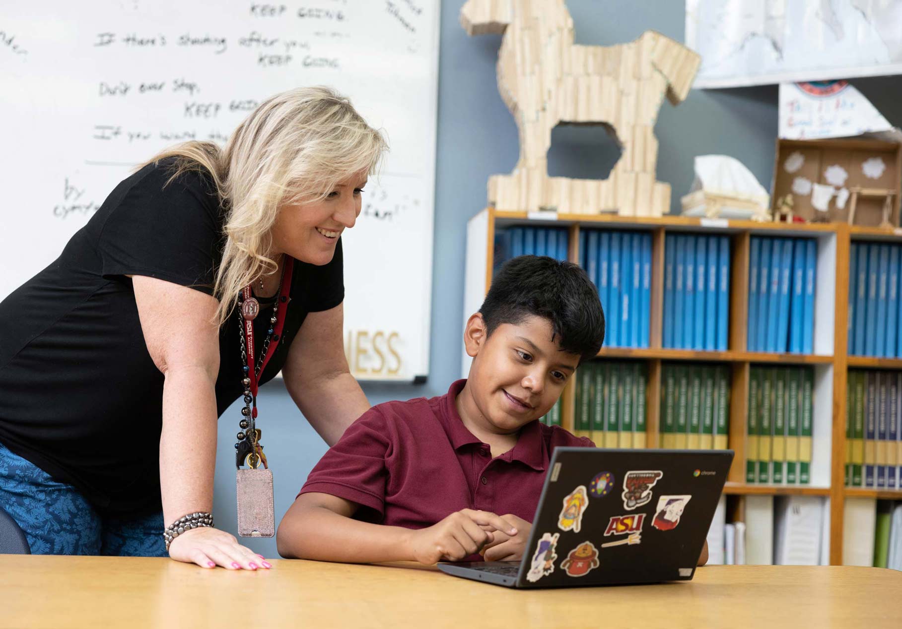 A teacher and young learner look at a laptop together in a classroom.