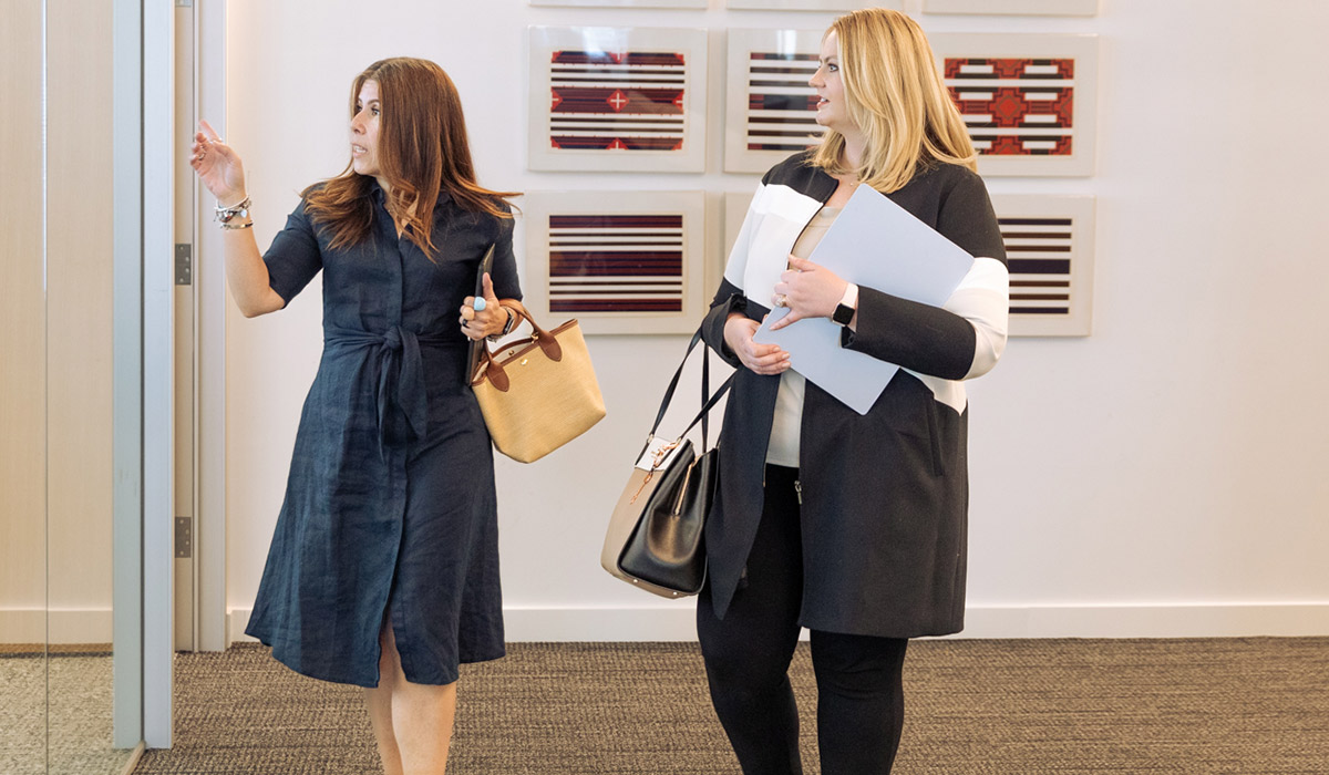 Two professional women converse in an office setting.
