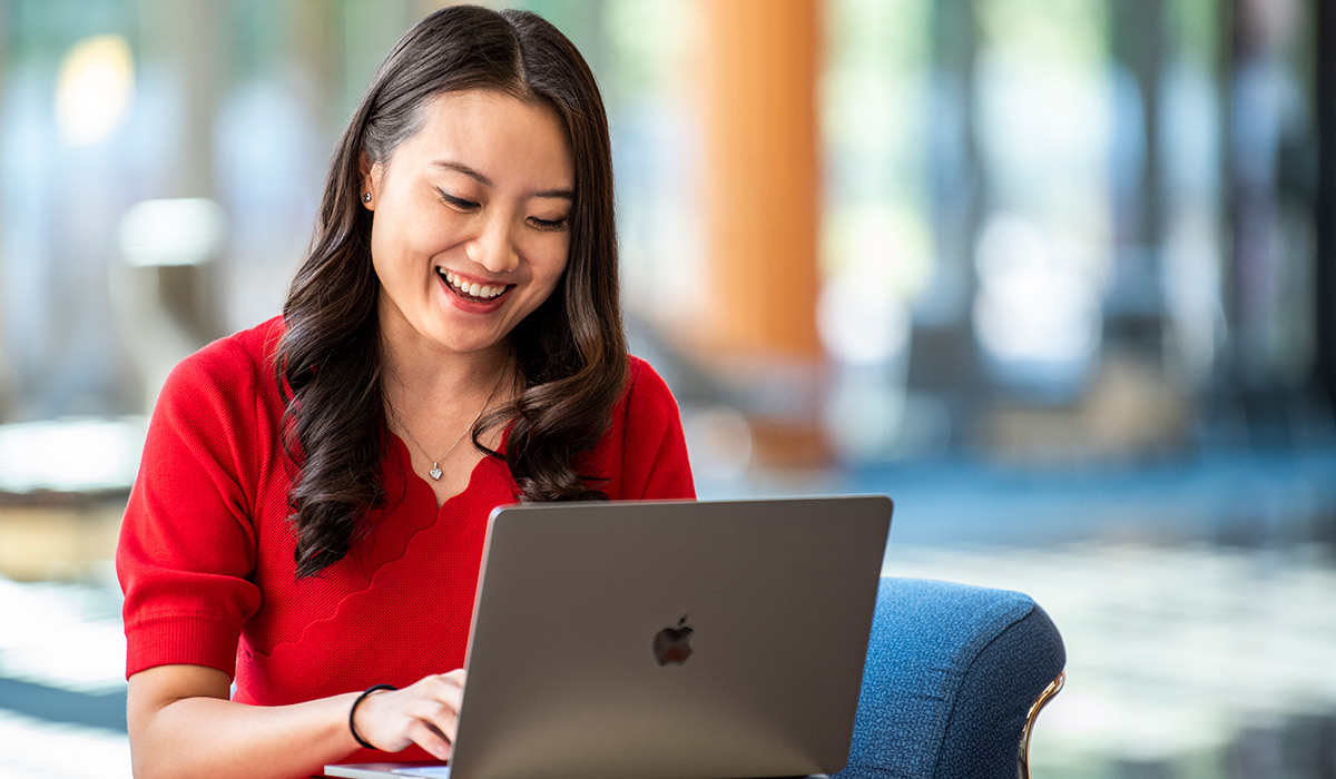 A woman wearing a red blouse smiles as she works on her laptop.