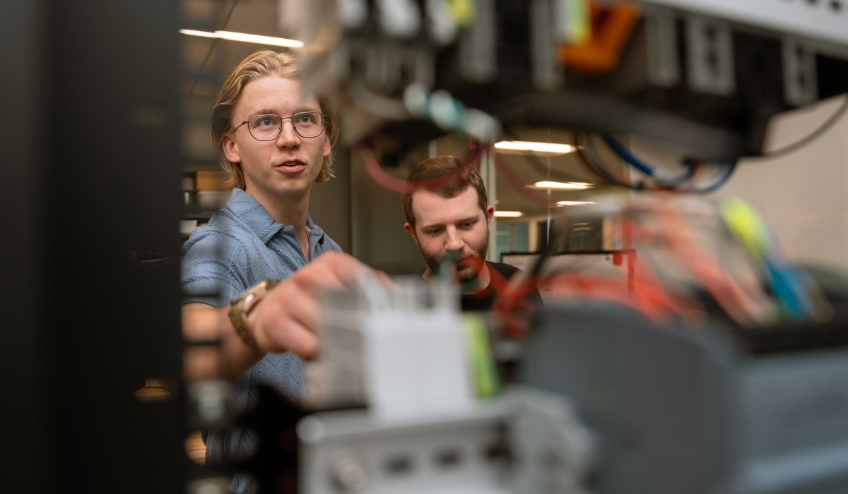 Two technologists with a management in technology degree examine hardware systems and equipment in a technical workspace.