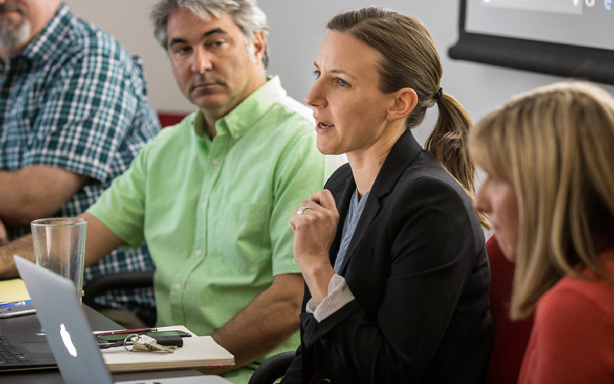 A group of executives sit at a table and talk about sustainability management practices.
