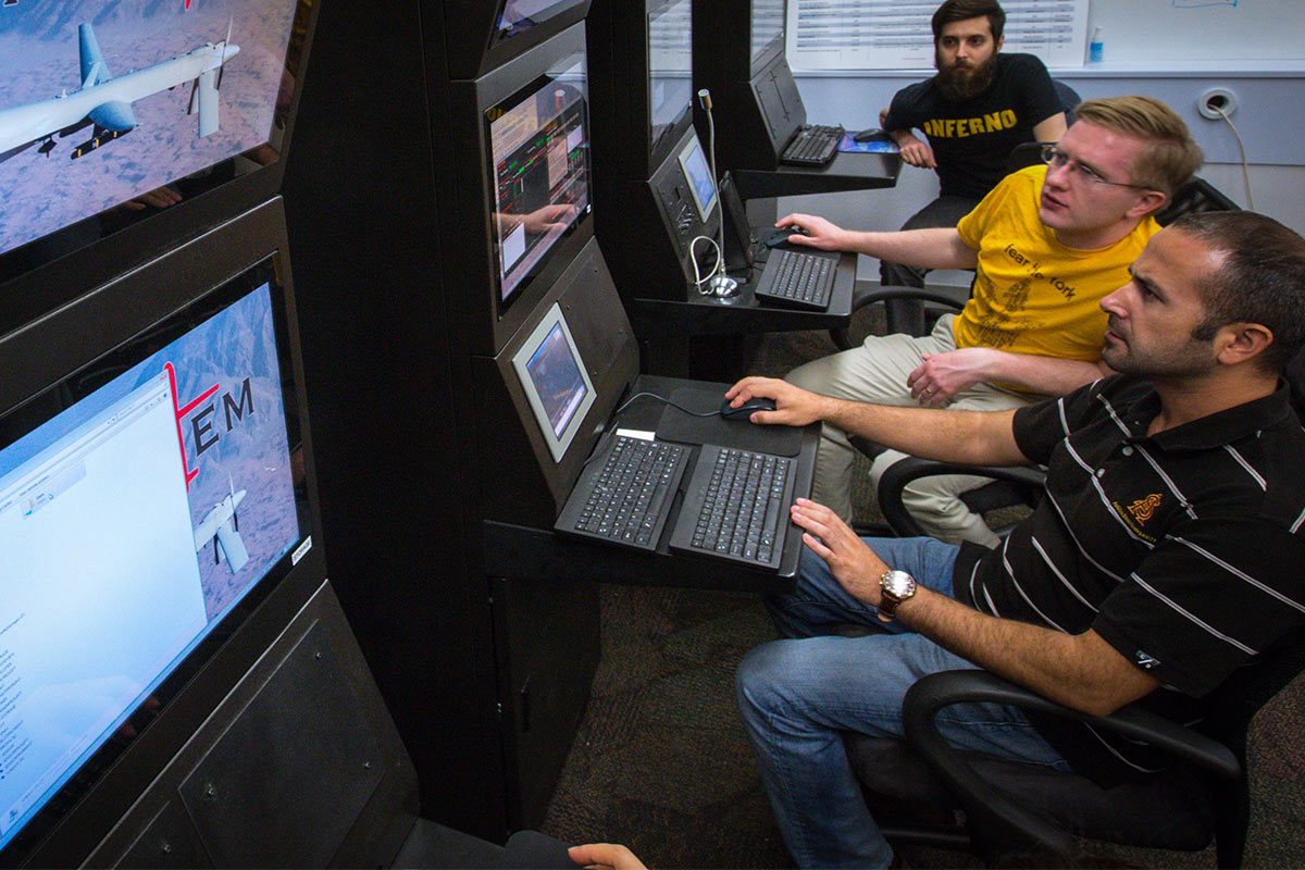 Three ASU students work on an airplane security program on several monitors.