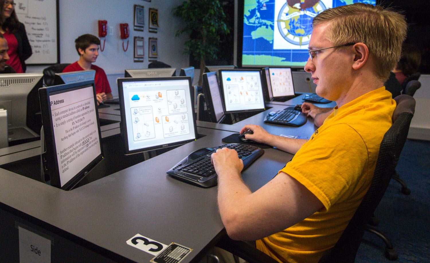 Students in the global cybersecurity program review course materials in a computer lab.